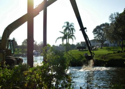 A barge-mounted long arm excavator removes shoaled material in a residential canal of the Manchester community